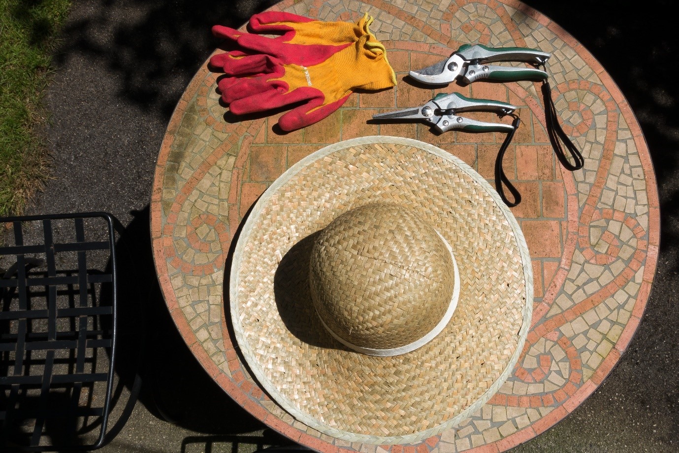 Slamený klobúk, záhradné rukavice a nožnice na mozaikovom stole 