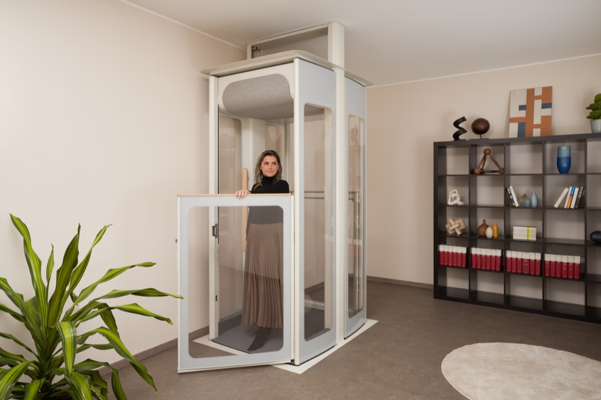Žena vo vnútri domáceho výťahu Stannah Uplifts s otvorenými dverami, ktorý sa vyznačuje priehľadnými bočnými stranami a kompaktnými rozmermi.