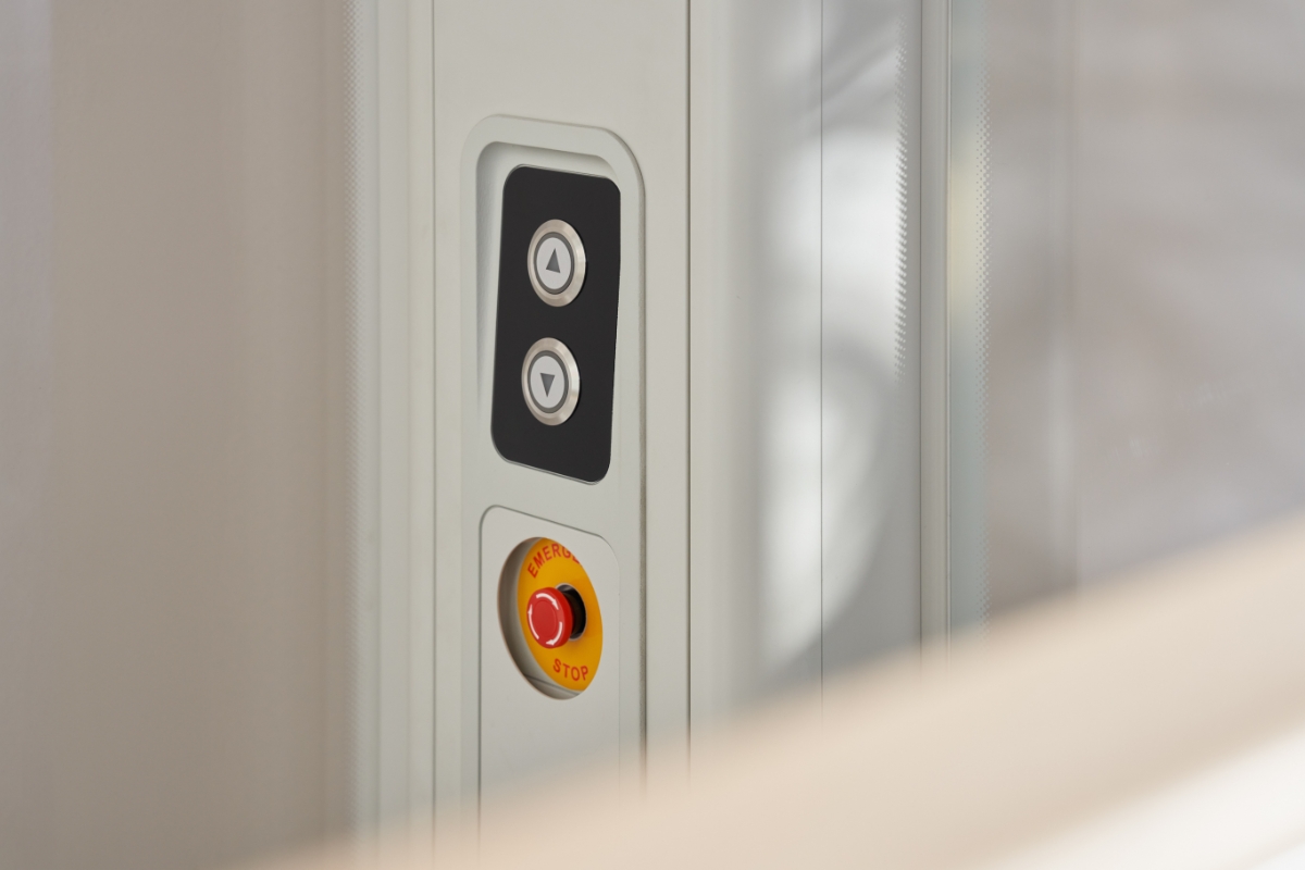 Detail ovládacieho panelu domáceho výťahu Stannah Uplifts s tlačidlami na jazdu hore a dolu a červeným tlačidlom núdzového zastavenia pre bezpečnú prevádzku.