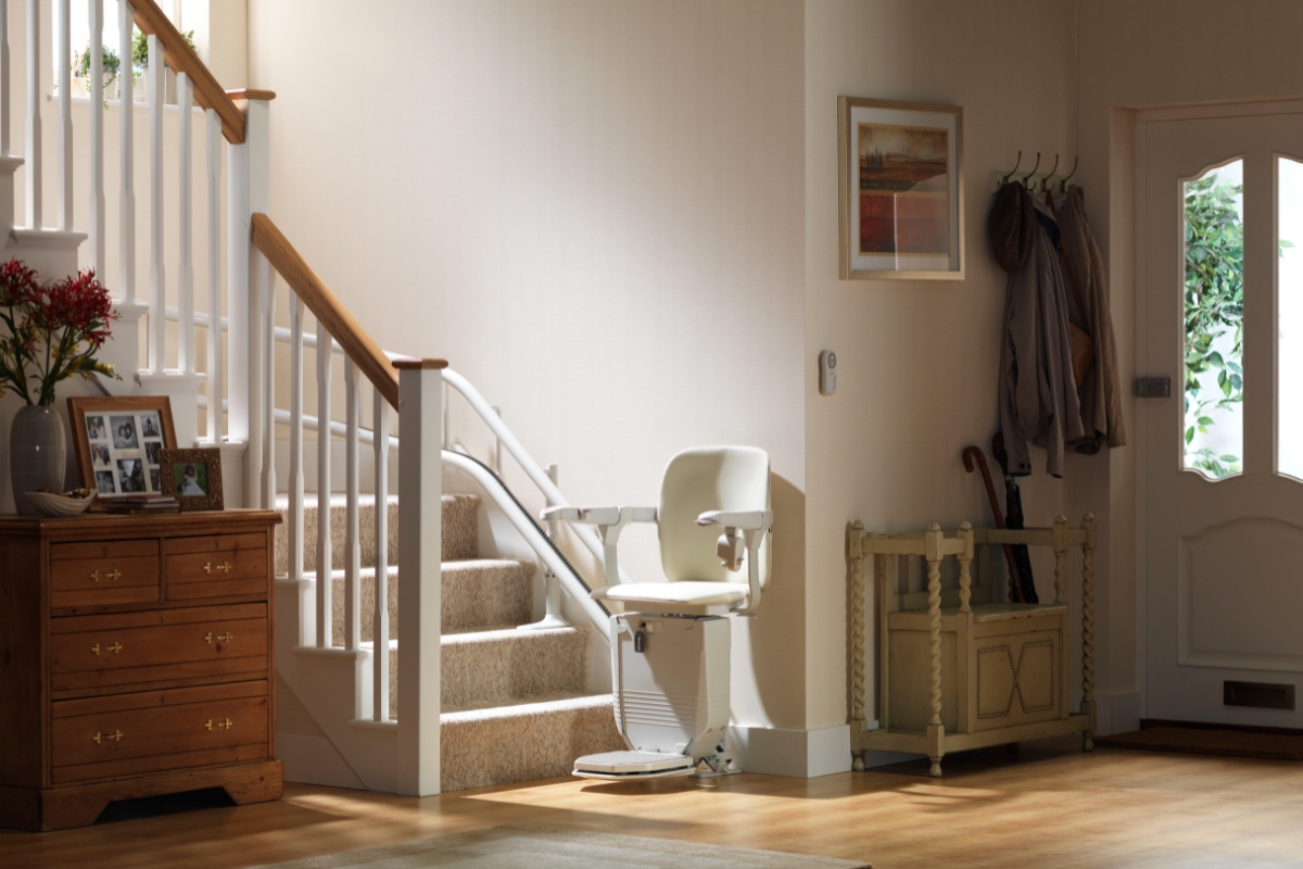 Béžový schodiskový výťah s zakrivenou koľajnicou inštalovaný pozdĺž schodiska v svetlej chodbe.